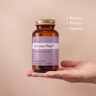An amber supplement bottle labeled 'Immune Hero' held in a person's hand against a soft beige background, with white text on the right reading 'Restore Protect Support'.